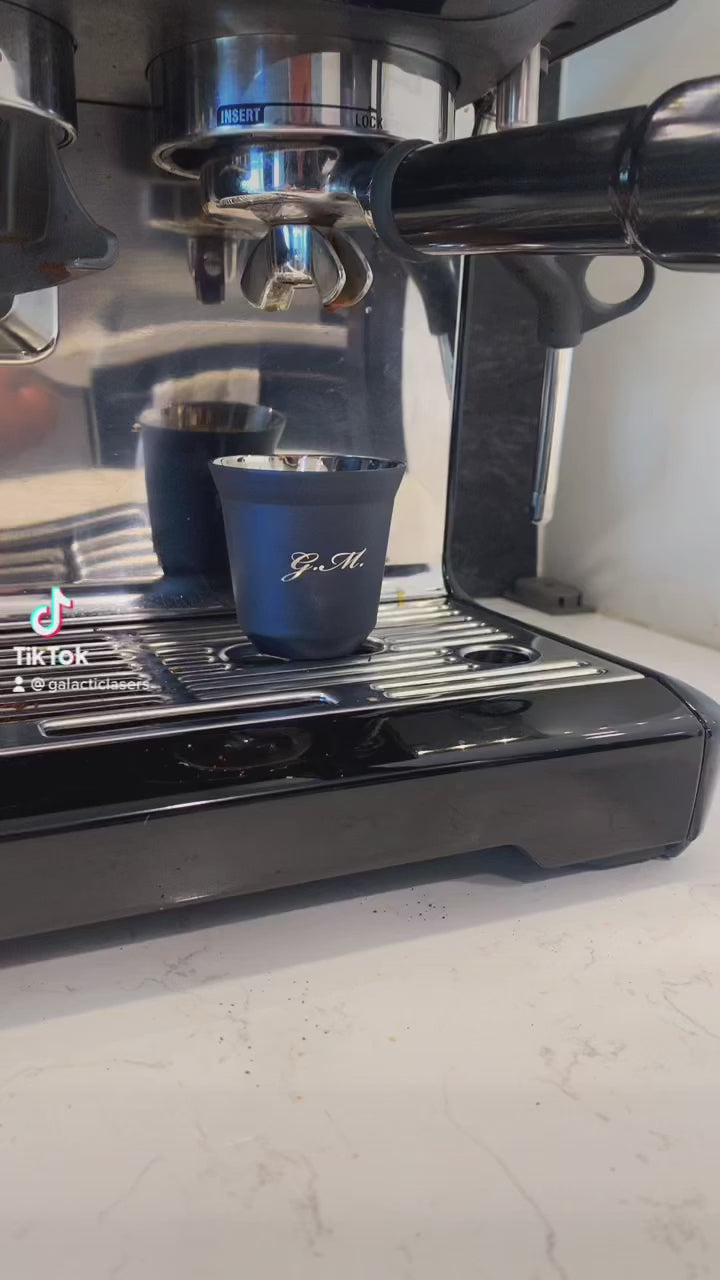 Navy Blue Engraved Single Stainless Steel Demitasse Espresso Cup 80ml with "G.M" engraved on the cup, showing a closeup of the cup include the espresso shot that is inside of the mug. This mug is on a breville barista express. - GalacticLasers